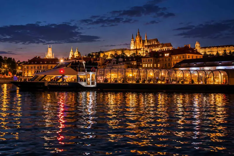 Prague at night and an illuminated glass boat on the Vltava